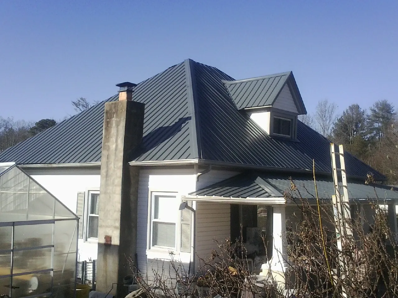 Dark blue standing seam metal roof on a white farmhouse with dormer — Slate & Tile Roof Repair by Roofing Brothers in Onley