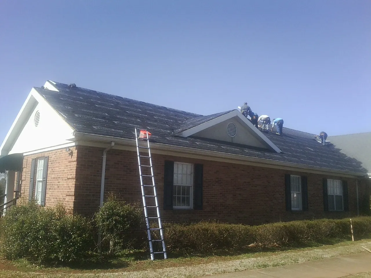 Crew tearing shingles off a brick ranch roof with a ladder set — Emergency Roof Repair work by our crew in Onley