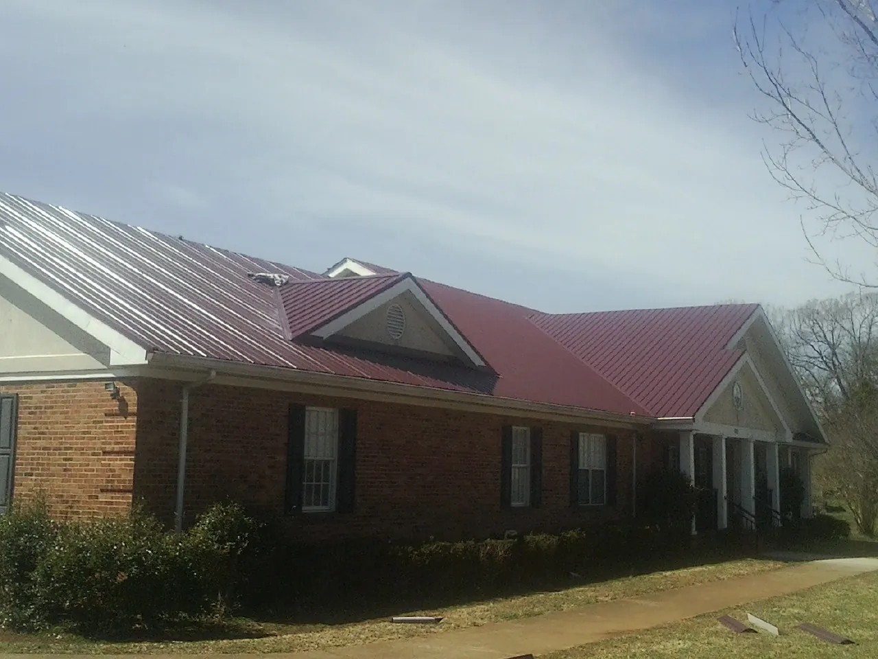 Red metal roof with gabled entries on a long brick building, from a Hail Damage Roof Repair job in Onley