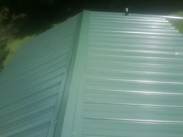 New green metal panels meeting at the ridge of a roof — Flat Roof Repair work by our crew in Onley