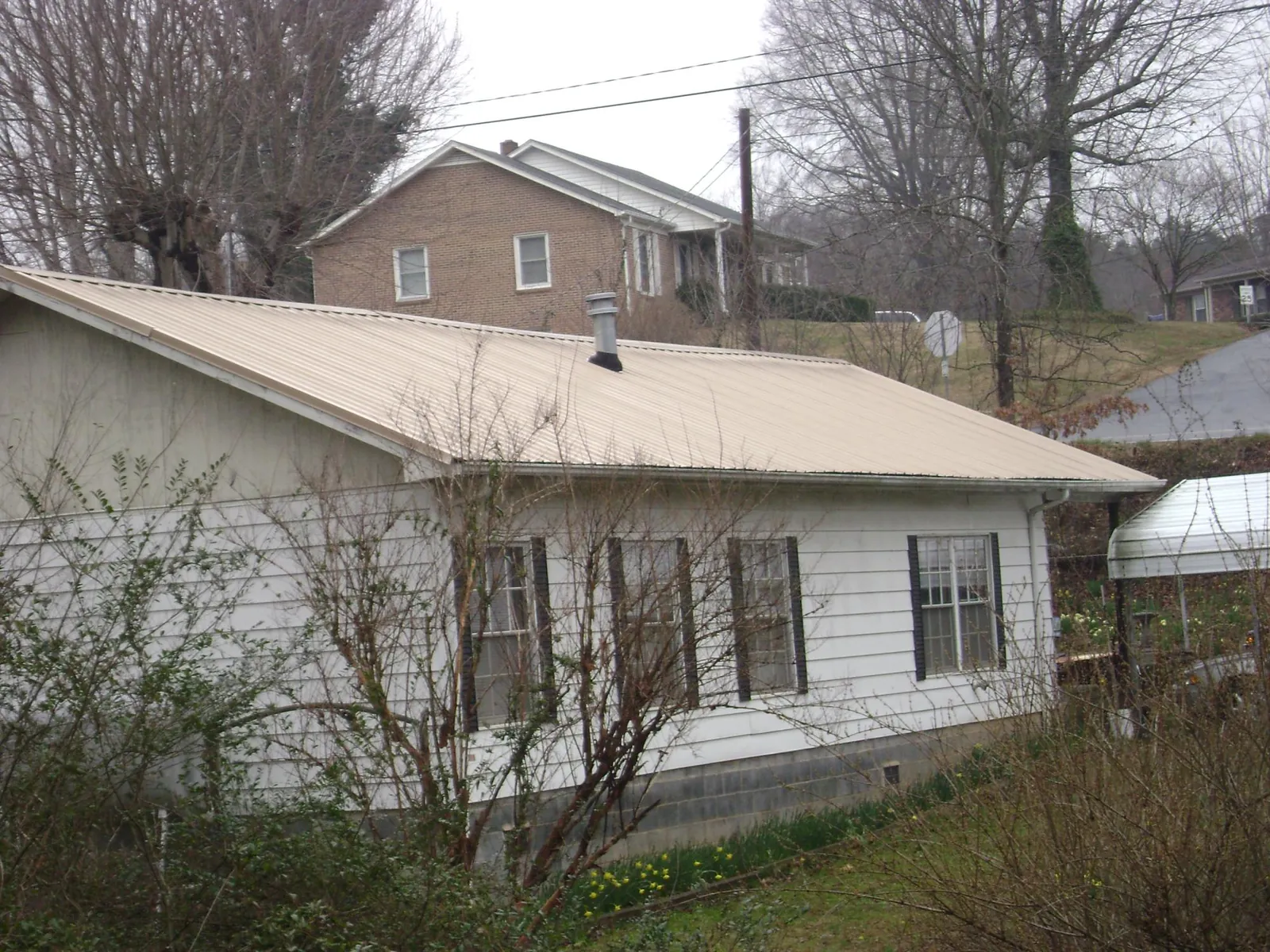 Tan metal roof on a white sided house set into a hillside — Commercial Roofing by Roofing Brothers in Onley
